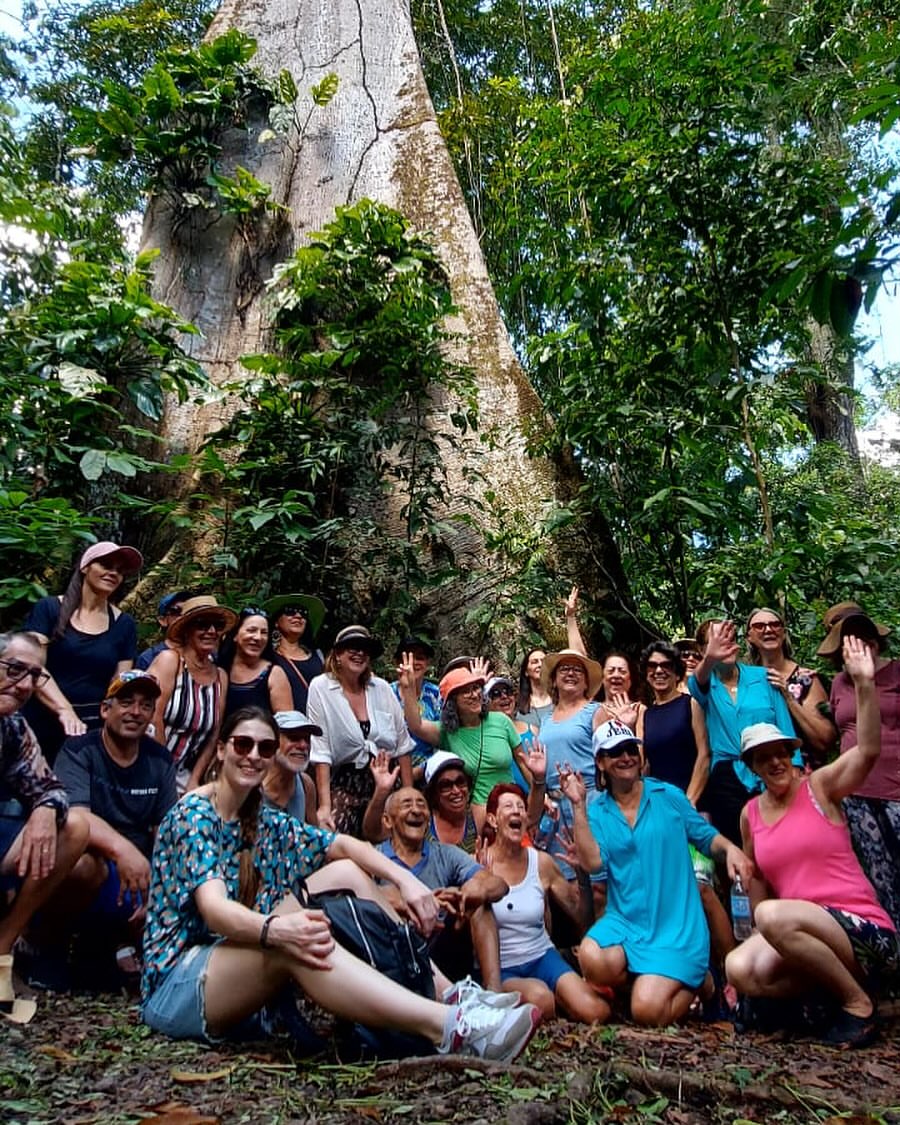 Grupo sorrindo sob uma árvore gigante na floresta do Pará